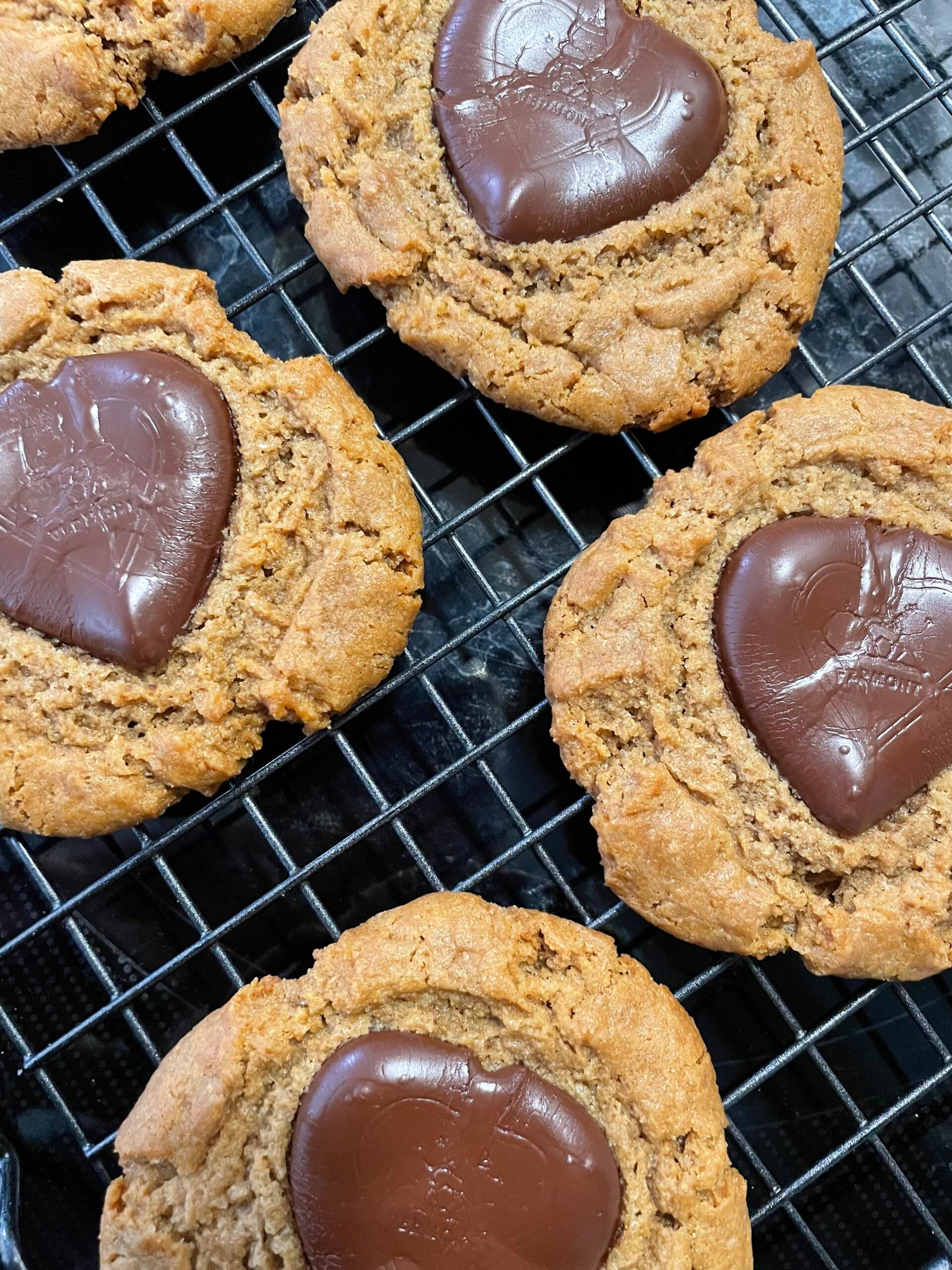 Peanut butter blossom cookies with heart-shaped chocolate candies on a black wire cooling rack